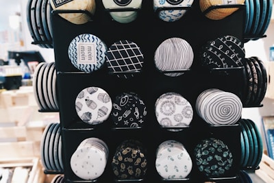 A display featuring rows of round decorative buttons with various black and white patterns, including geometrical shapes, abstract designs, and symbols. The buttons are neatly arranged on a stand with a variety of designs that feature typography, spirals, and wave patterns.