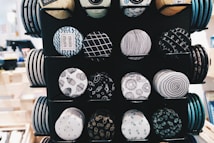 A display featuring rows of round decorative buttons with various black and white patterns, including geometrical shapes, abstract designs, and symbols. The buttons are neatly arranged on a stand with a variety of designs that feature typography, spirals, and wave patterns.