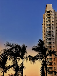 A high-rise residential building with balconies overlooking lush gardens and Dubai’s skyline at sunset.
