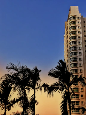 Tall residential building with balconies and sunset in the background.