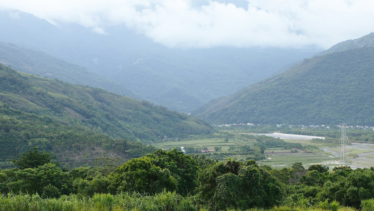 花蓮山區俯瞰溪谷，山腳下是田野與聚落，山頭有雲霧