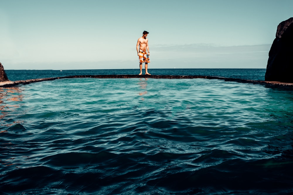 man in brown shorts standing on rock in the middle of sea during daytime