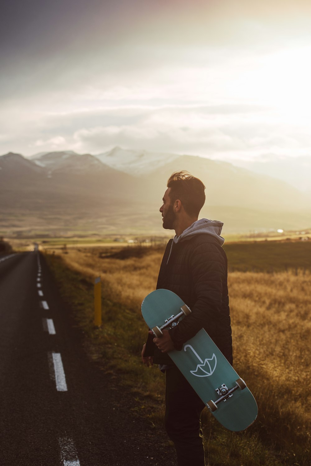 Mann in schwarzer Jacke und blauer Jeans sitzt tagsüber auf schwarzem Skateboard auf der Straße