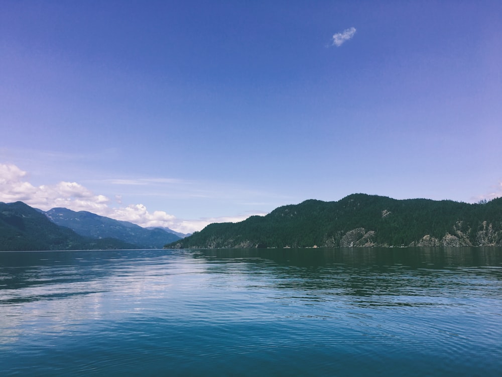 green lake near green mountains under blue sky during daytime