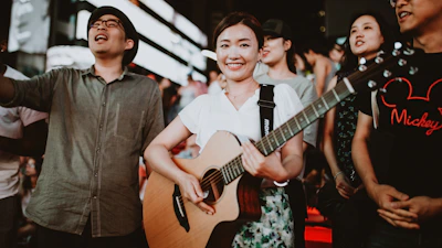 A group of teenagers playing guitar and smiling outdoors during a music workshop.