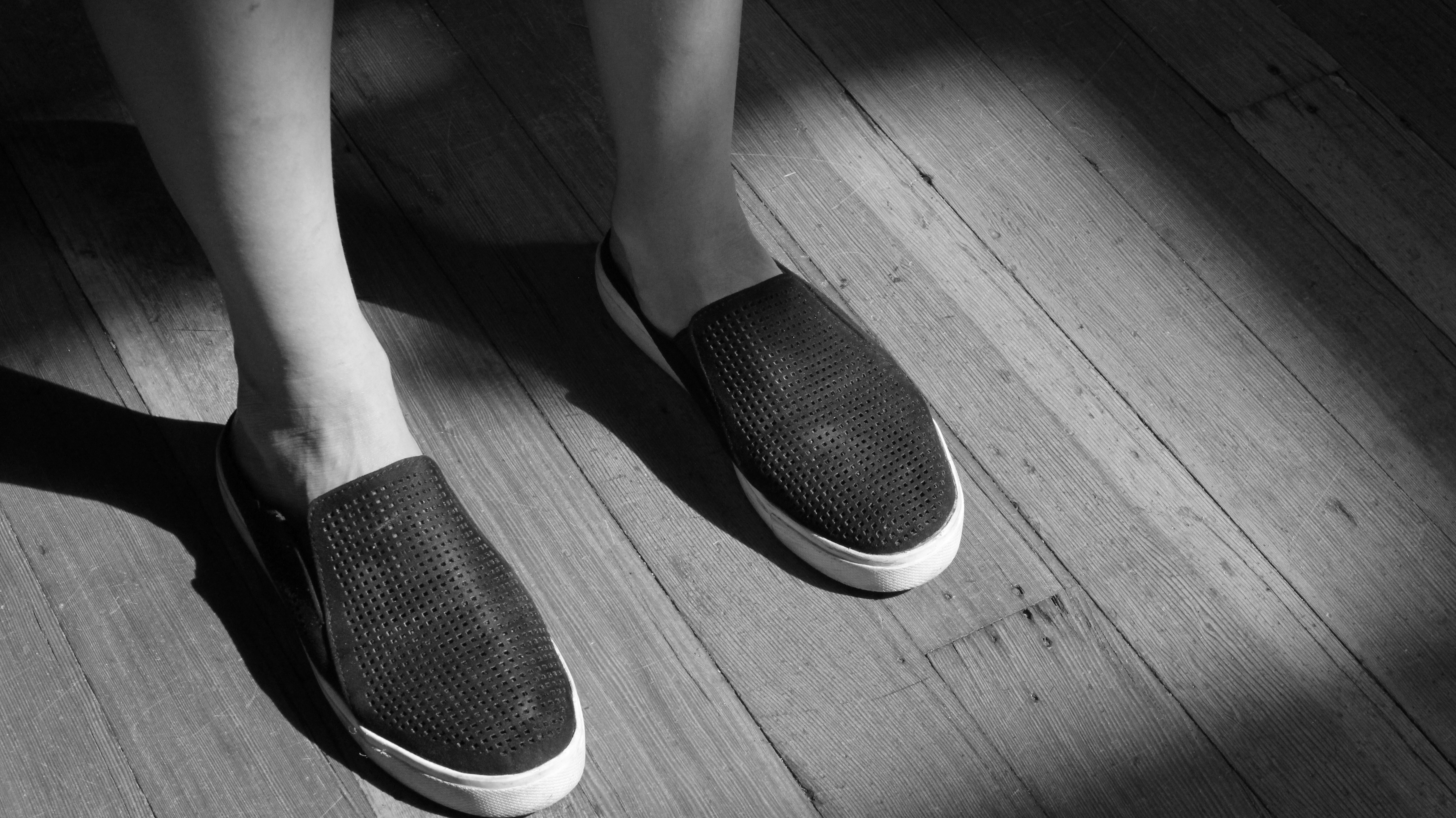 Dark polished leather shoes on a wooden floor, dramatic side lighting, luxury footwear close-up