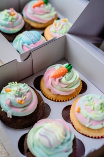 Colorful cupcakes in soft pastel wrappers displayed in a rustic wooden box with subtle flour dusting