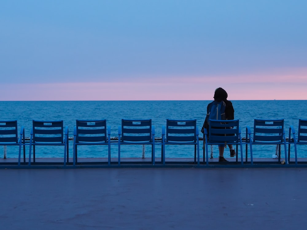 pessoa sentada no banco de madeira azul na praia durante o dia