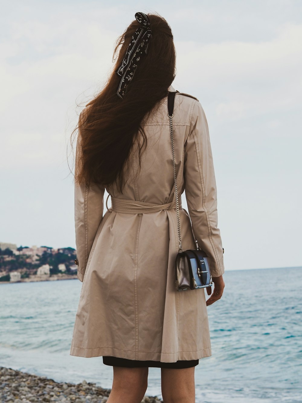 昼間、海辺に立つ茶色のコートを着た女性