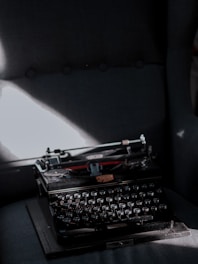 Dark moody image of an old typewriter with shadowy figures in the background.