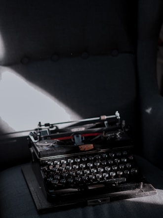 Dark moody image of an old typewriter with shadowy figures in the background.
