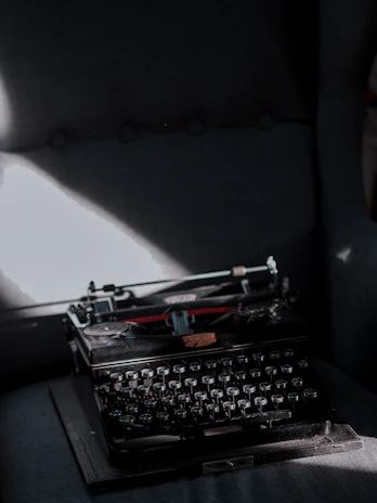 A dimly lit vintage typewriter with soft golden light casting shadows on dark velvet fabric.