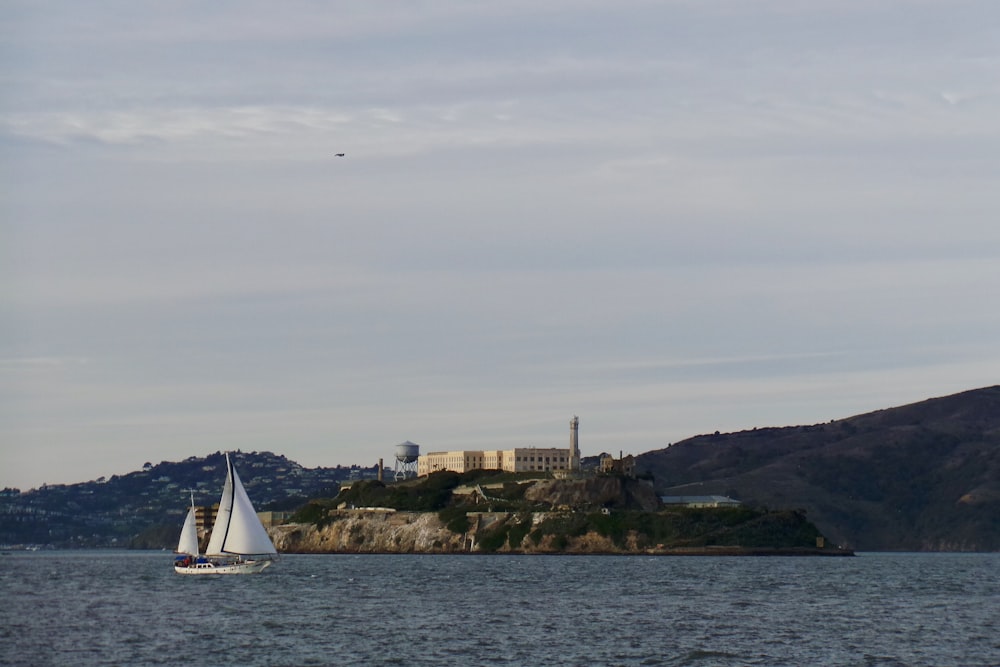 white sailboat on sea near brown and green mountain under white clouds during daytime