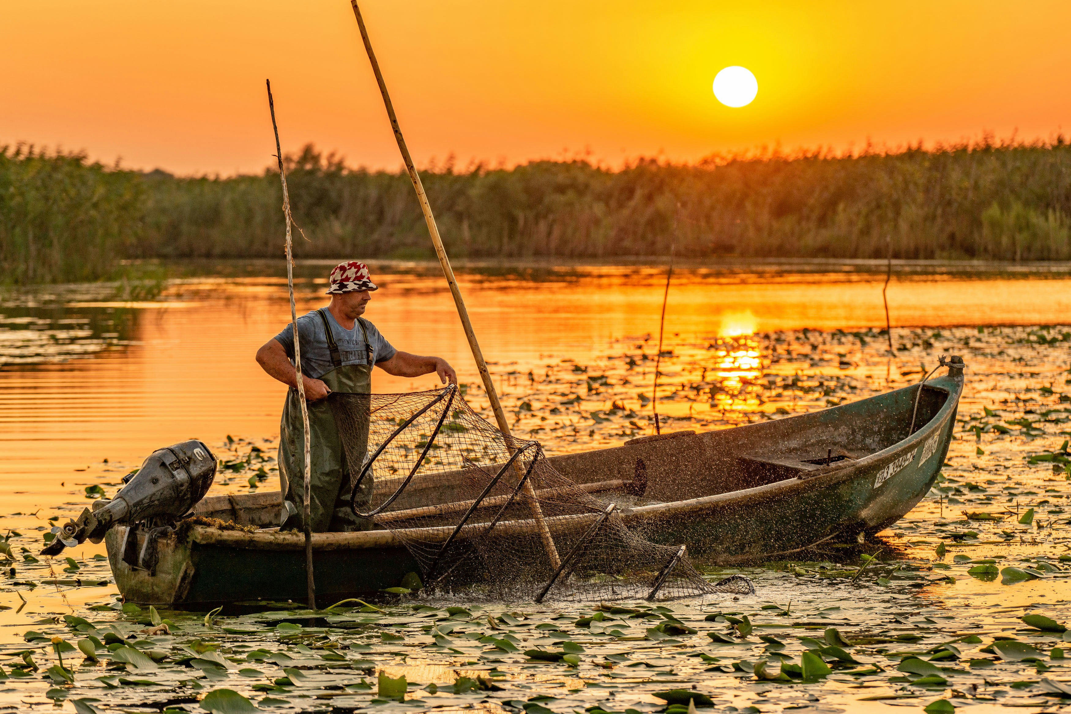 man in blue t-shirt sitting on brown wooden boat during sunset