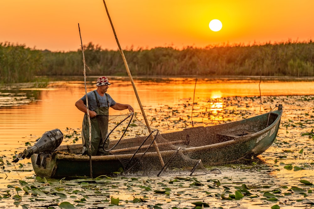man in blue t-shirt sitting on brown wooden boat during sunset