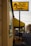 A rental business with a prominent yellow sign displaying the name 'Sun Rental Center' is featured. The building’s exterior wall is painted yellow, matching the sign and awning. There's a small piece of heavy machinery parked near the building, and a main road extends into the distance on the right side of the image with a few vehicles.