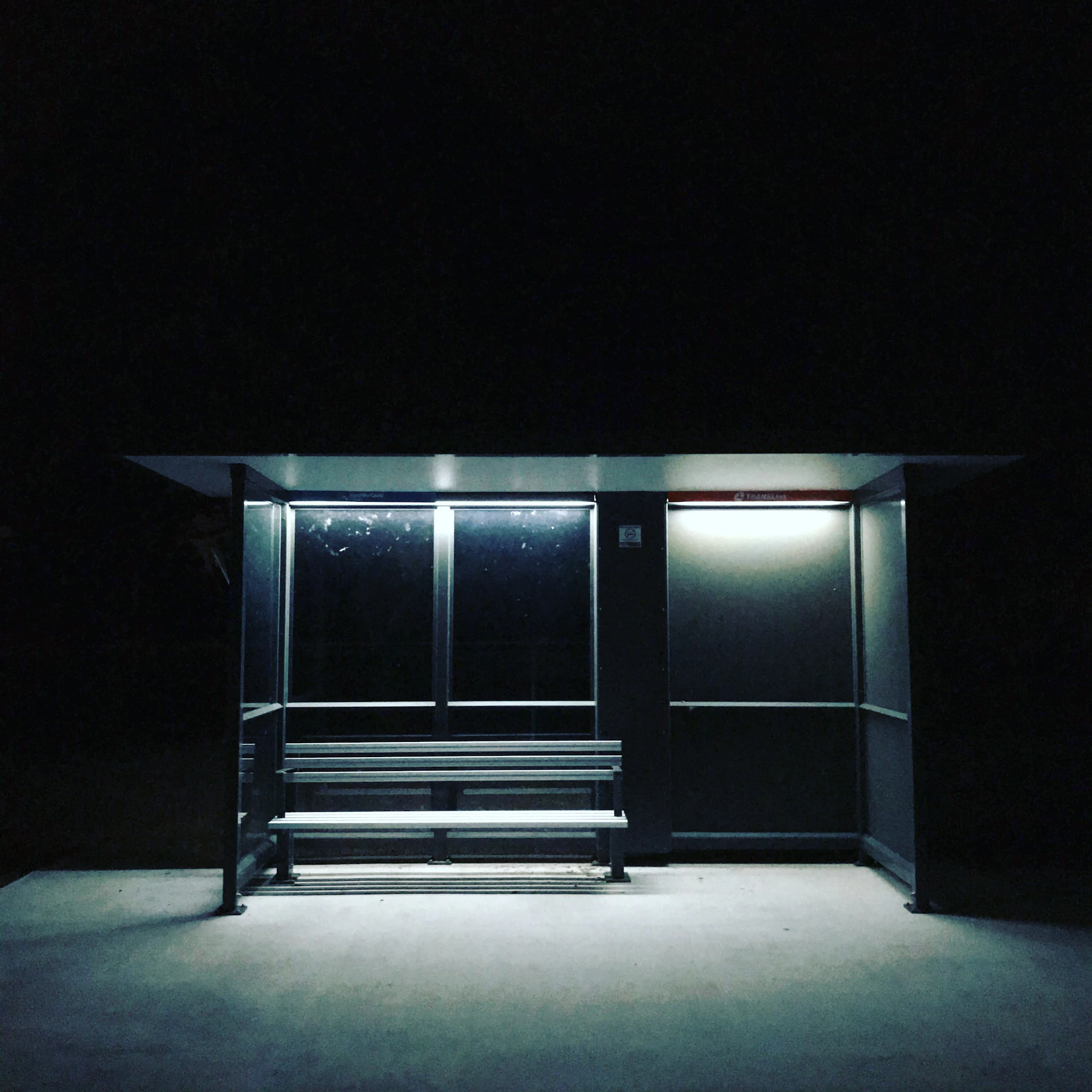A lit bus shelter standing alone on a dark street at night