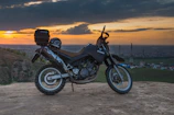 Sunset silhouette of a motorcycle parked on a hilltop overlooking the city.