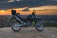 A rugged motorcycle parked on a rocky trail at sunset, gear strapped securely.