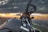 A close-up view of a Yamaha motorcycle with its handle and a part of the chassis visible against a backdrop of a picturesque sunset. The horizon shows a landscape that includes hills and a distant town or city under a sky filled with dramatic clouds.