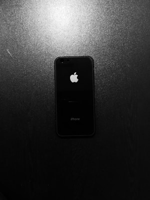A black smartphone with a prominent white Apple logo, placed on a textured dark surface.