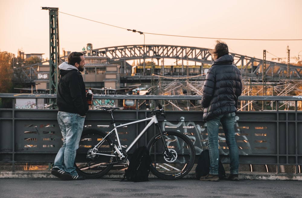 man in black jacket and blue denim jeans standing beside black motorcycle during daytime