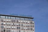 A modern building with multiple windows graced by the inscription 'Leibniz Universität' in blue lettering on its roof. The sky is clear and blue, creating a serene backdrop.