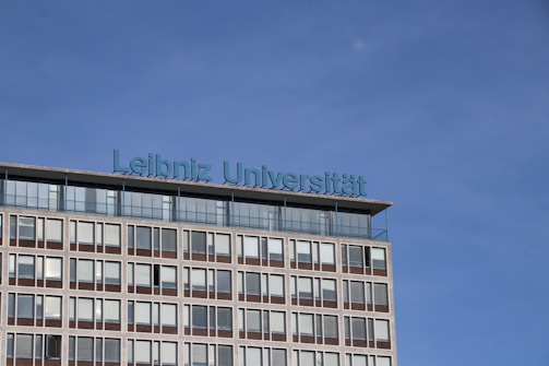 A modern building with multiple windows graced by the inscription 'Leibniz Universität' in blue lettering on its roof. The sky is clear and blue, creating a serene backdrop.
