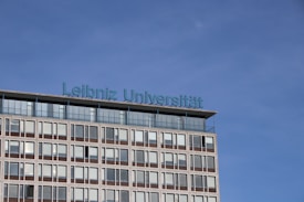 A modern building with multiple windows graced by the inscription 'Leibniz Universität' in blue lettering on its roof. The sky is clear and blue, creating a serene backdrop.