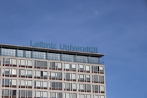 A modern building with multiple windows graced by the inscription 'Leibniz Universität' in blue lettering on its roof. The sky is clear and blue, creating a serene backdrop.
