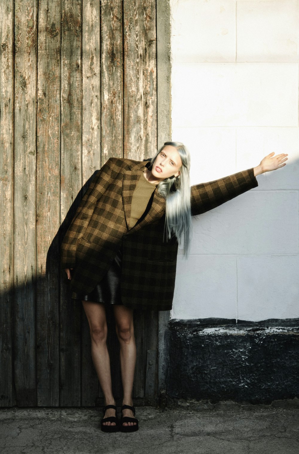 woman in black and brown plaid coat standing beside brown wooden wall