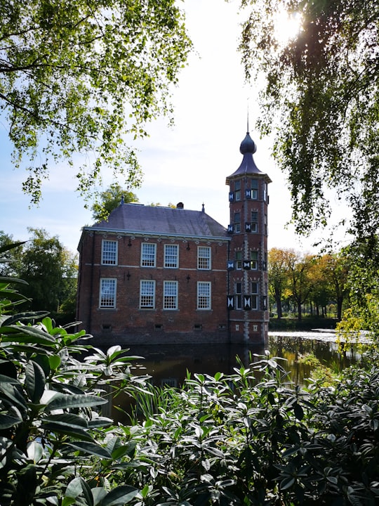 brown concrete building near green trees and river during daytime in Kasteel Bouvigne Netherlands
