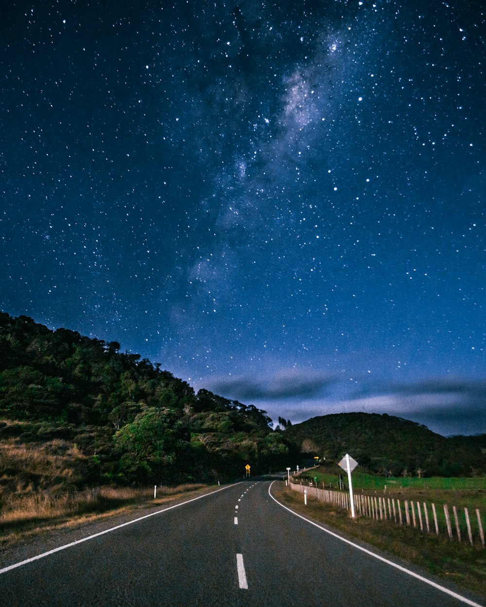 gray concrete road between green grass field under blue sky during night time