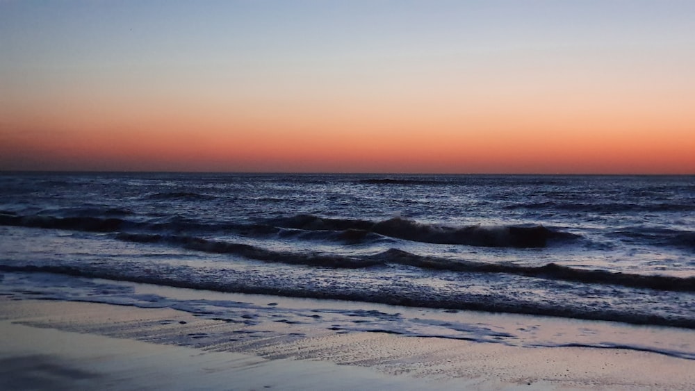 ocean waves crashing on shore during sunset