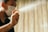 A person wearing a mask sprays a fine mist from a bottle. The background is softly blurred, drawing attention to the hand and the spray.