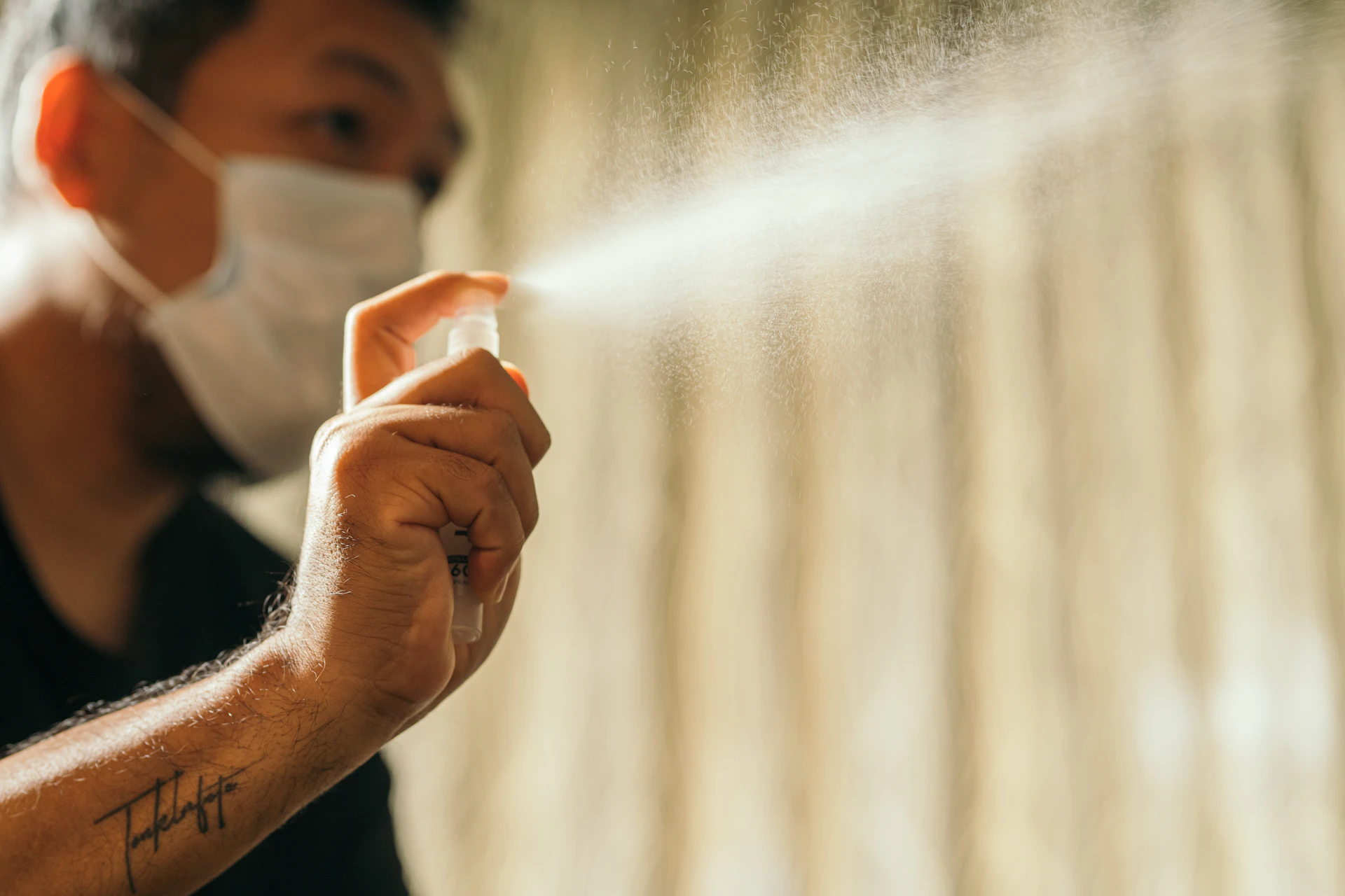 Close-up of a hand spraying a luxurious perfume mist, with golden particles sparkling in the air against a neutral-toned background.