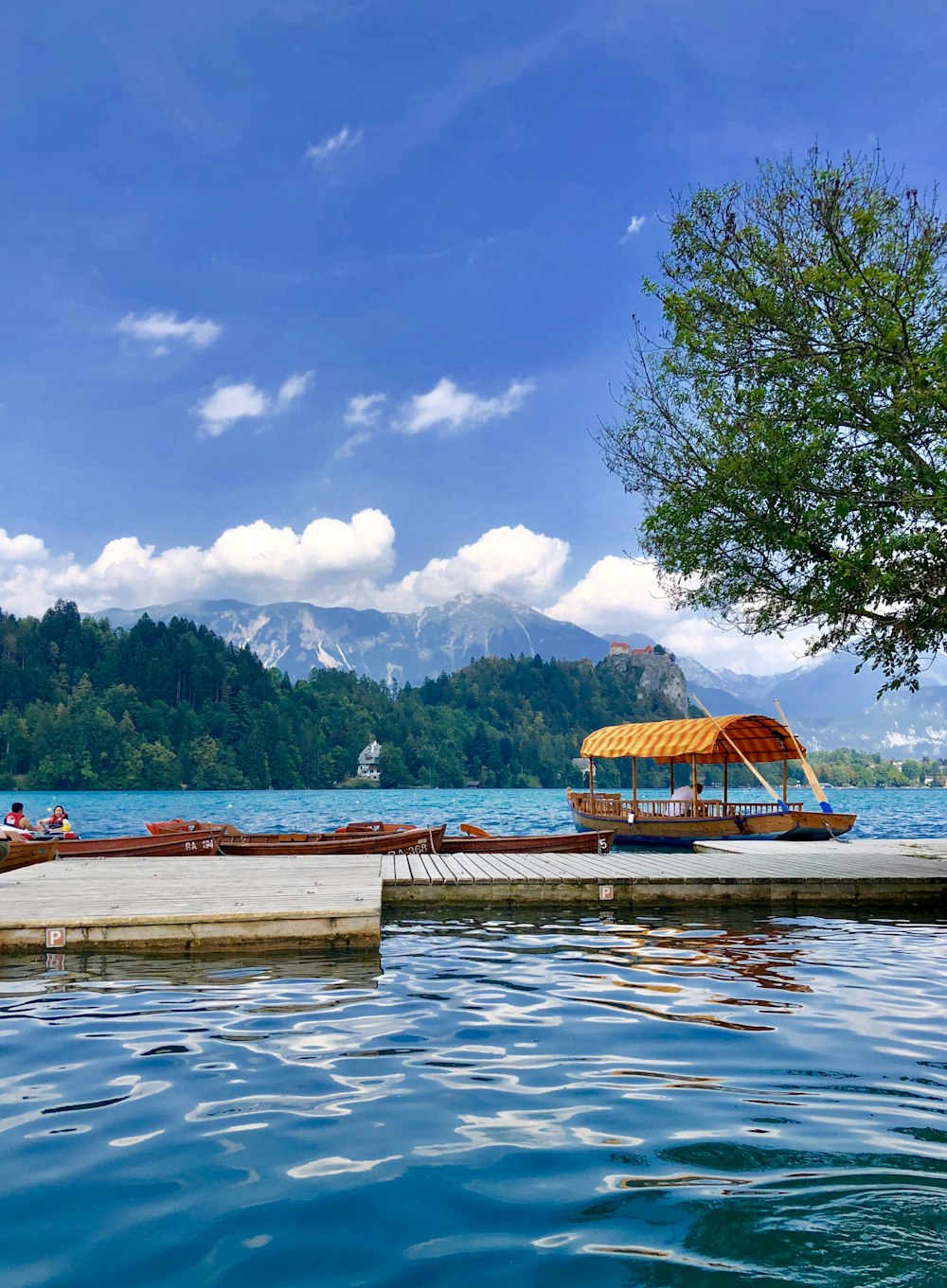 doca de madeira marrom no lago perto da montanha verde sob o céu azul e nuvens brancas durante o dia