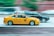 A yellow taxi and a black SUV are driving side by side on a road, with motion blur emphasizing their speed. The taxi has an advertisement on top and showcases iconic NYC taxi markings.