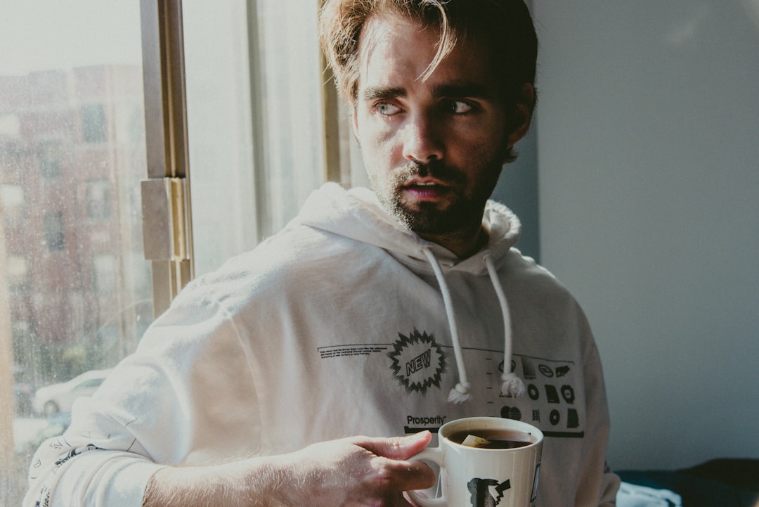 man in white hoodie holding white ceramic mug
