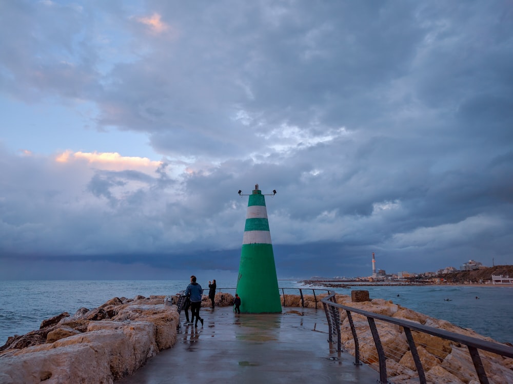 green and white lighthouse near body of water under cloudy sky during daytime