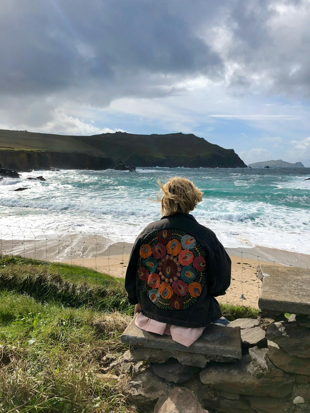 woman in black and gray jacket sitting on gray concrete bench looking at the sea during