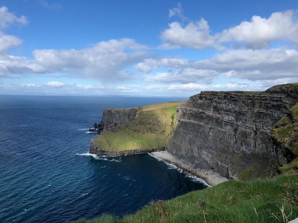 green and brown mountain beside body of water under blue sky during daytime