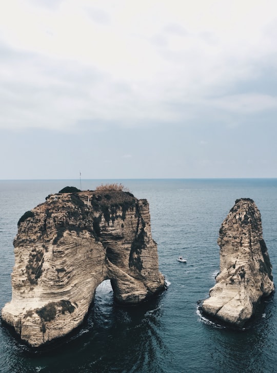 brown rock formation on sea under white clouds during daytime in Raouche Rocks Lebanon
