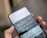 A hand is holding a smartphone displaying the 9gag app with a humorous text post about using the app repeatedly. The app's interface includes tabs and options for memes and funny content.