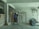 A person is carrying a bag of cement on their shoulder inside a storage room. The room contains several stacks of cement bags and a pile of metal rods or wire. The walls and floor are concrete, and there is minimal lighting with an exposed light fixture hanging from the ceiling.