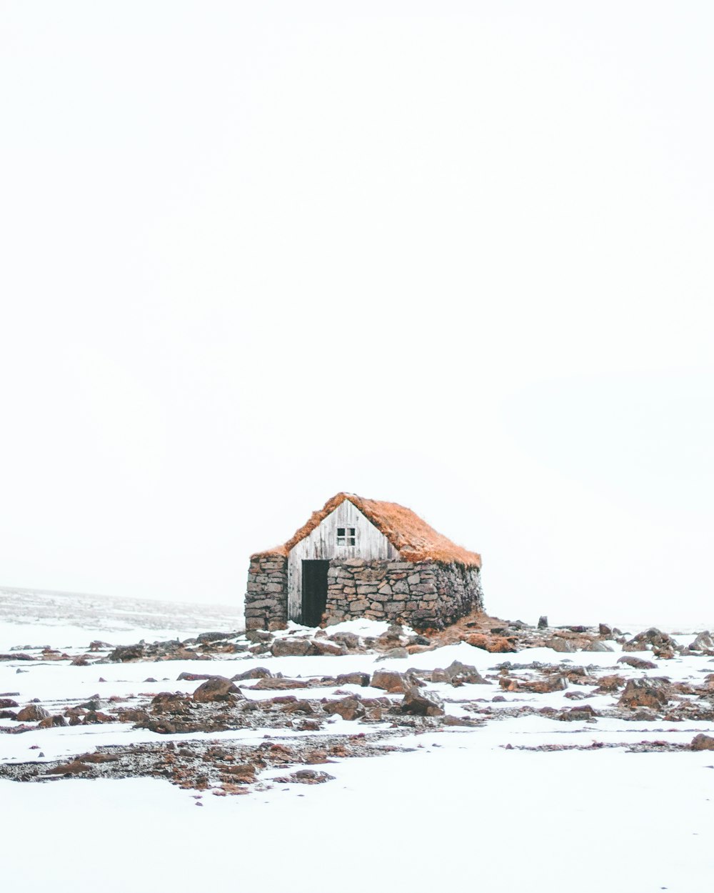 Braunes Holzhaus auf schneebedecktem Boden unter weißem Himmel tagsüber