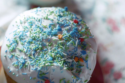 Close-up of a hand decorating a cake with colorful frosting and sprinkles.