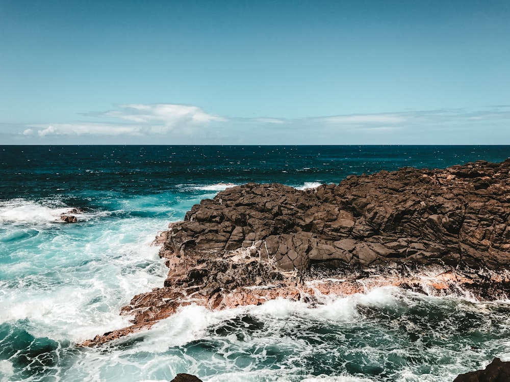 brown rock formation on sea under blue sky during daytime