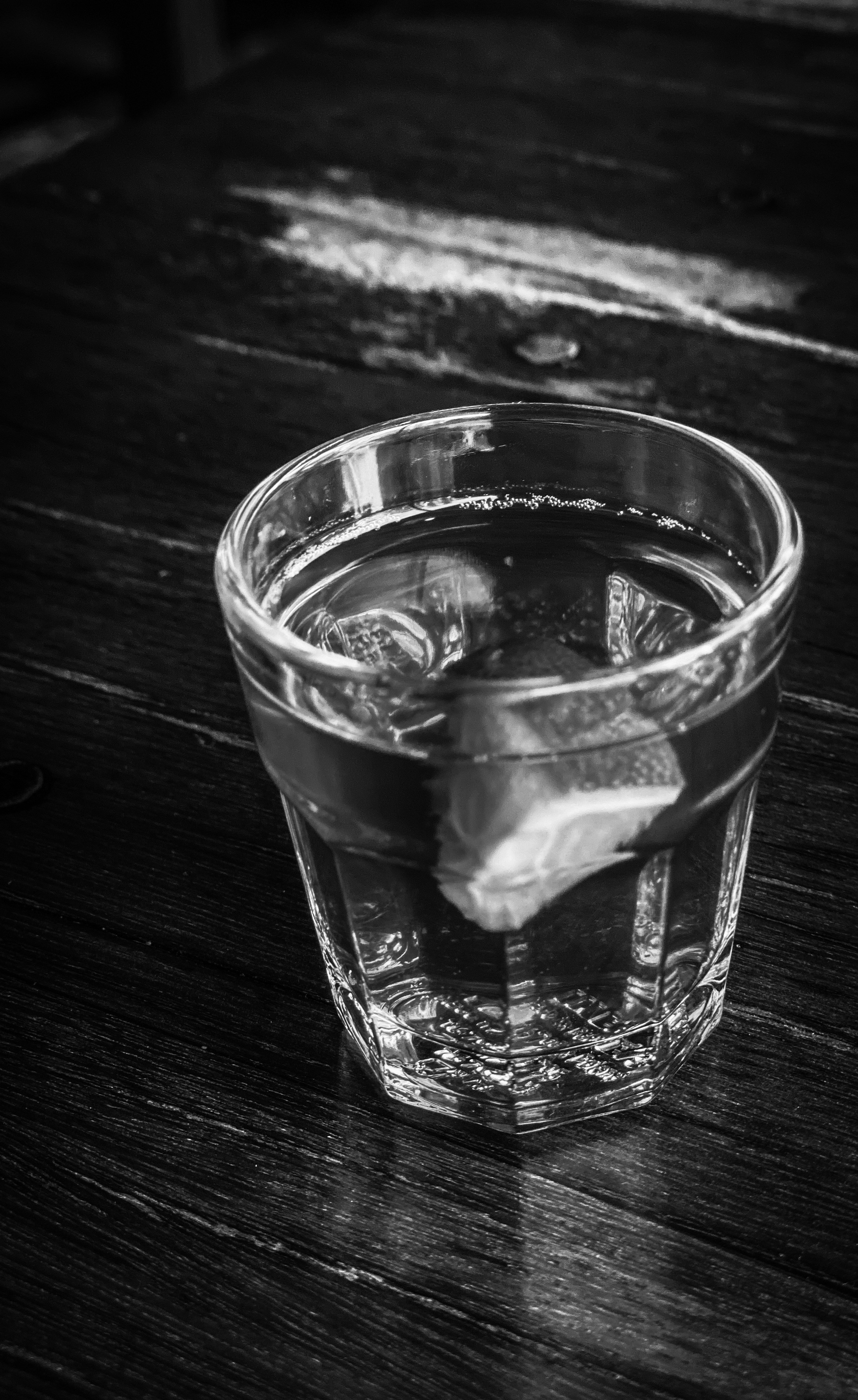Vaso de agua fresca con rodajas de limón sobre mesa de madera natural, luz matutina suave y cálida, entorno minimalista