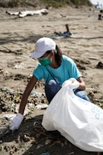 woman in blue t-shirt and white cap sitting on brown sand during daytime